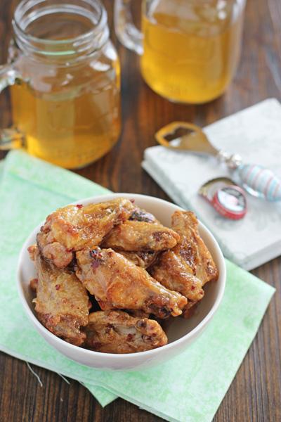 A bowl filled with Honey Chipotle Wings with two beers to the side.