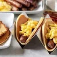 Two breakfast tacos in holders loaded with eggs, sausage, and syrup.