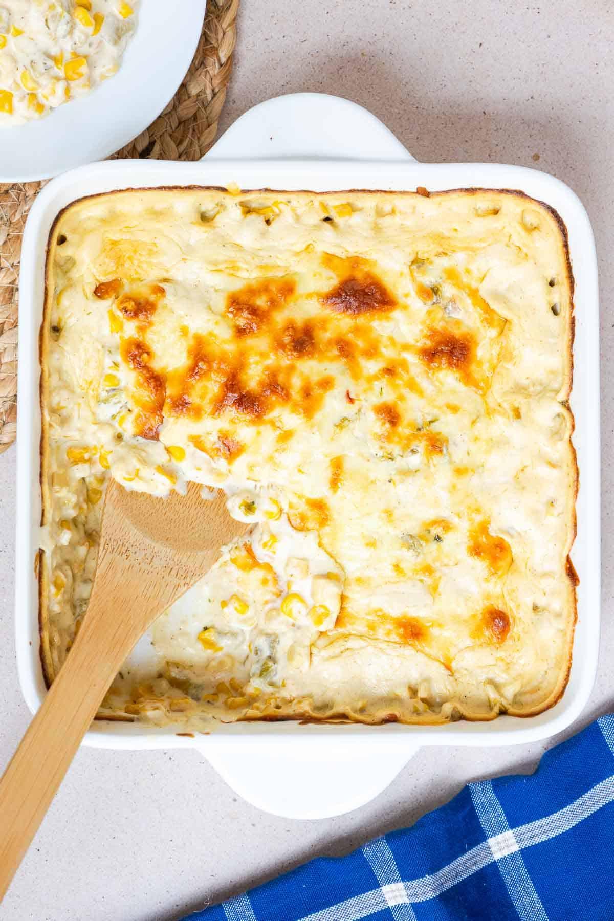A serving of Green Chile Corn Casserole is scooped out of the baking dish to show the creamy consistency.