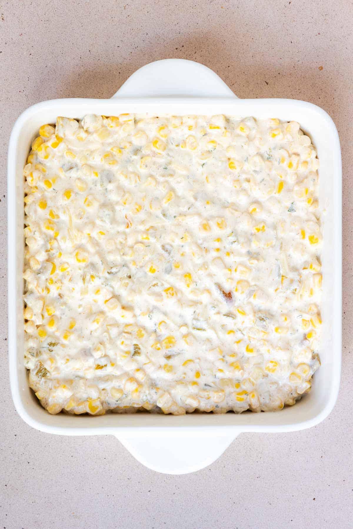 The corn casserole mixture is transferred to an 8 by 8 inch baking dish.