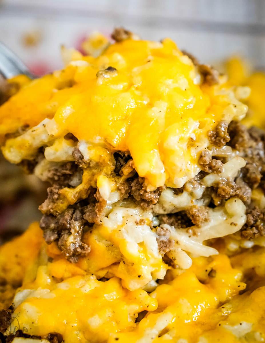 A scoop of cheesy Hamburger Hashbrown Casserole is lifted out of the pan.
