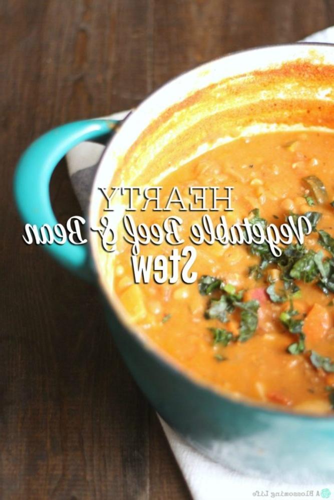 a large pot of beef and bean stew with potatoes, vegetables, ground beef in a turquoise dutch oven. Herbs are sprinkled over top