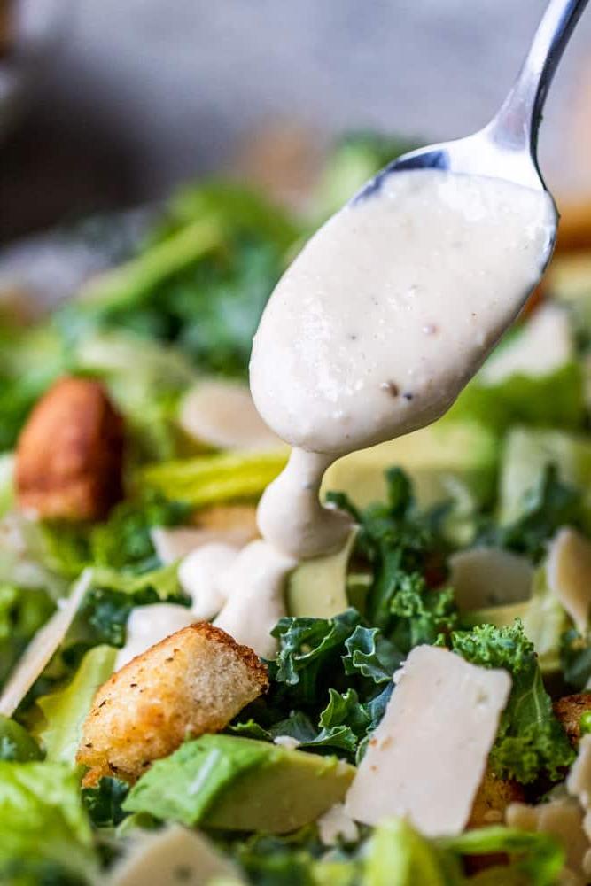 Silver spoon dripping dressing on salad.