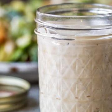 Caesar dressing in mason jar with salad in the background.
