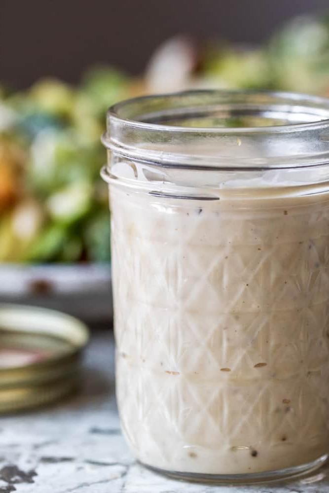 Caesar dressing in mason jar with salad in the background.