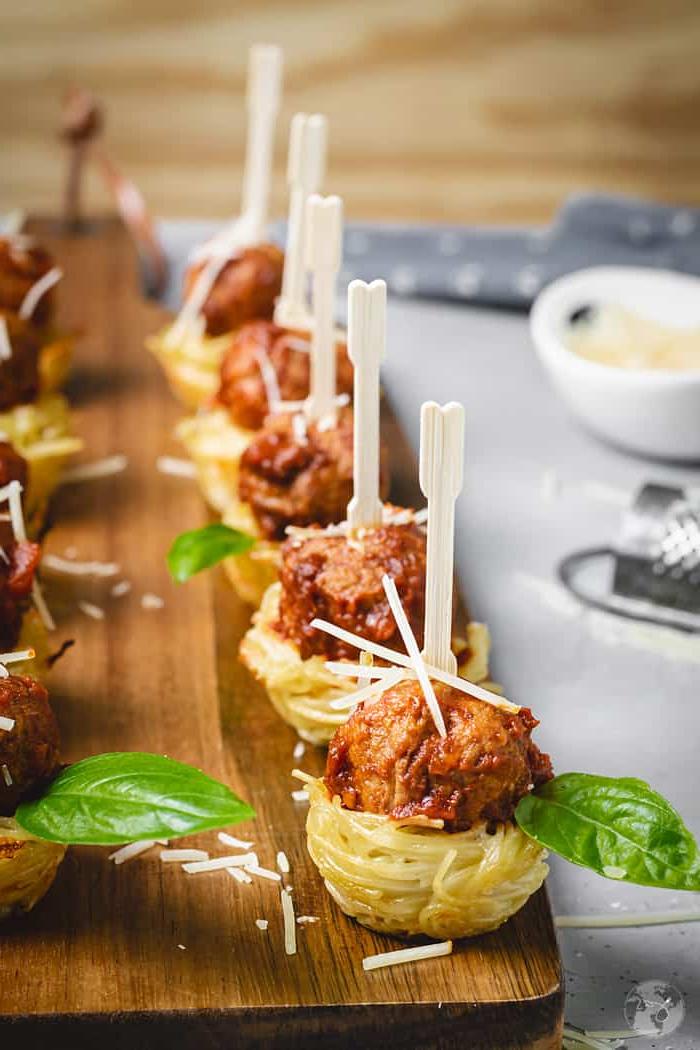 Meatball and spaghetti appetizer nests lined on a wooden board.