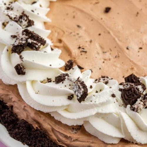 A closeup of a full gluten free Oreo mud pie topped with whipped cream swirls and crushed gluten-free Oreos.