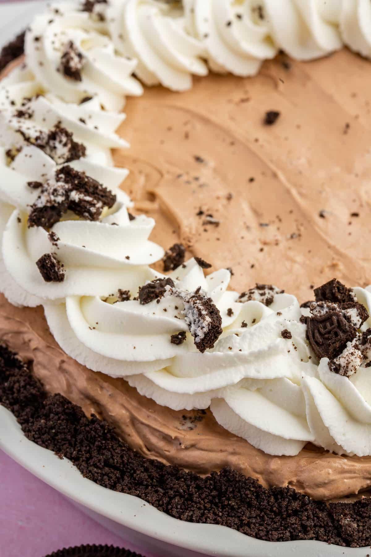 A closeup of a full gluten free Oreo mud pie topped with whipped cream swirls and crushed gluten-free Oreos.