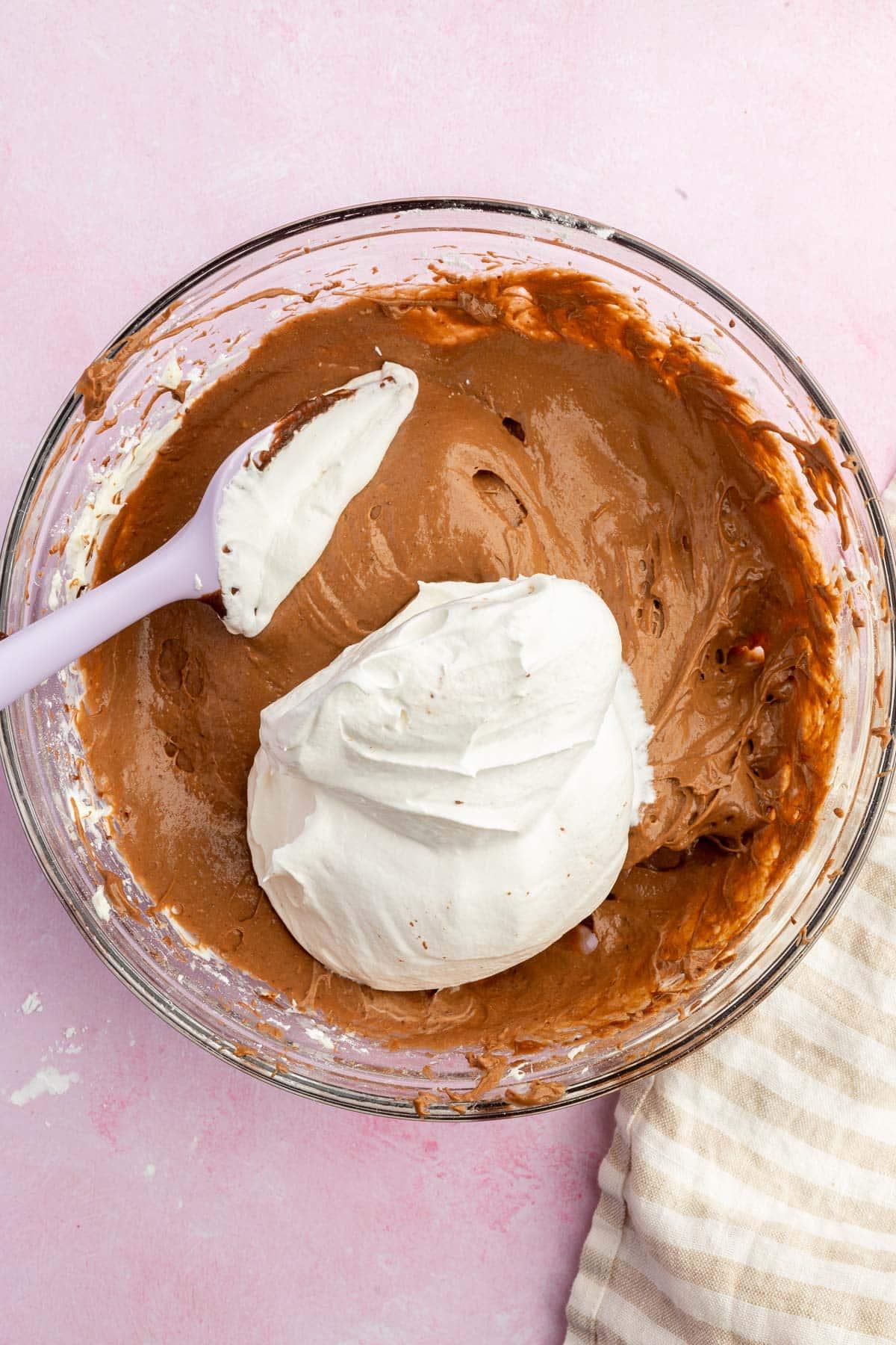 A glass mixing bowl with a chocolate pudding mixture topped with a large dollop of fresh whipped cream.