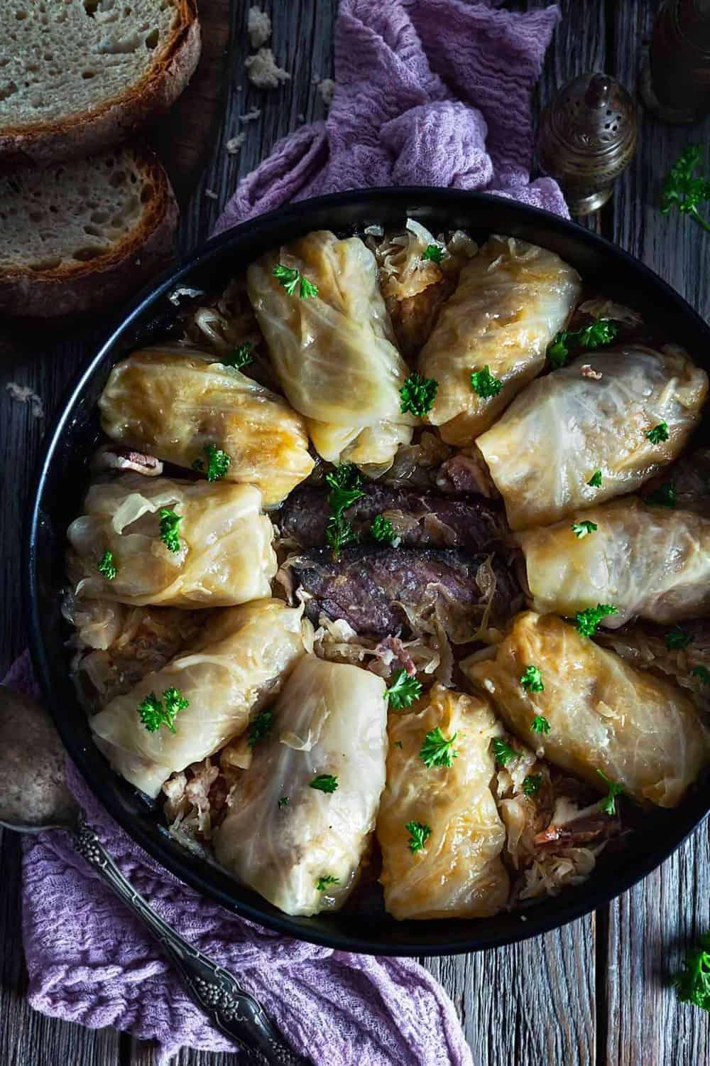An overhead photo of cabbage rolls placed in a circle in a round dish with smoked meat in the middle.